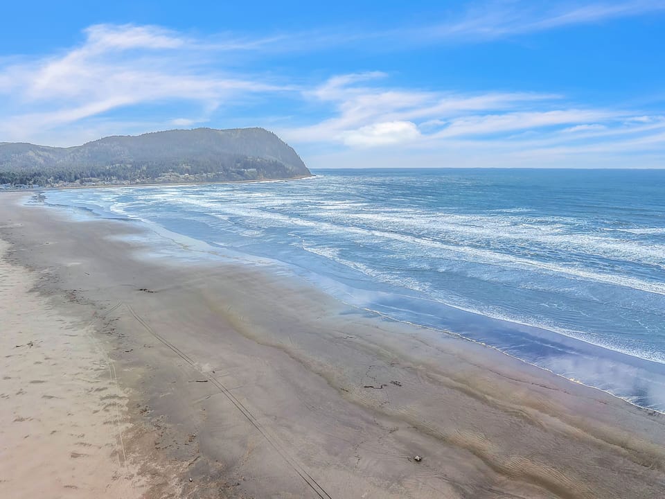 Pristine sandy shoreline meets rolling waves beneath dramatic coastal bluffs and endless blue skies.