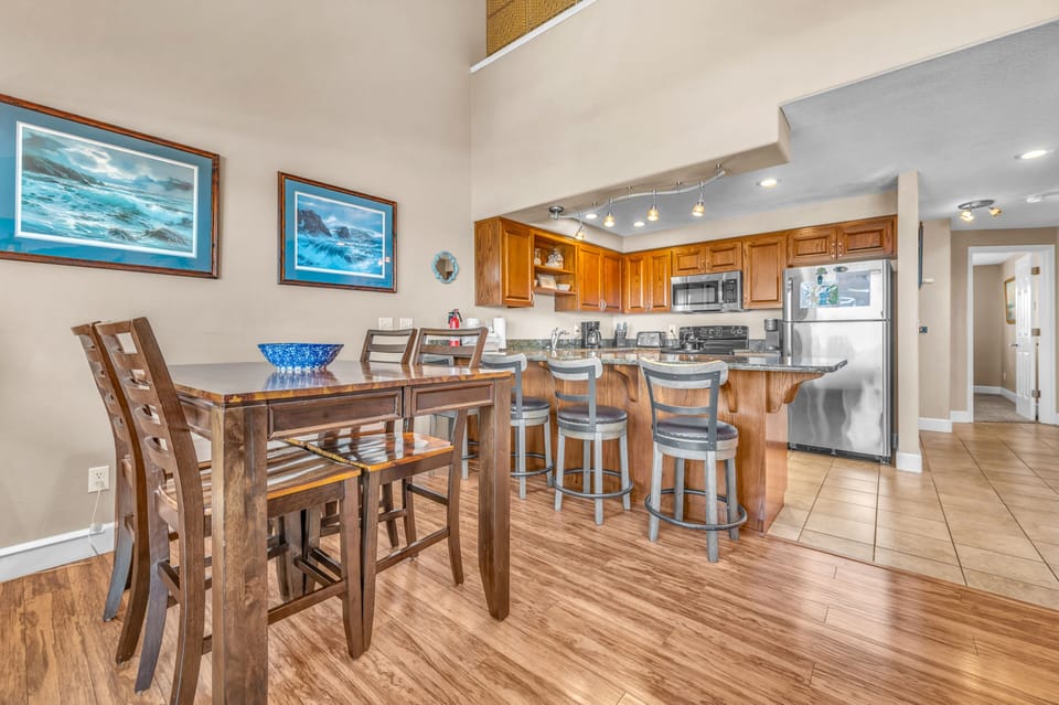 Your open-concept kitchen and dining space welcomes you with warm wood tones and coastal artwork, perfect for preparing meals and gathering together.