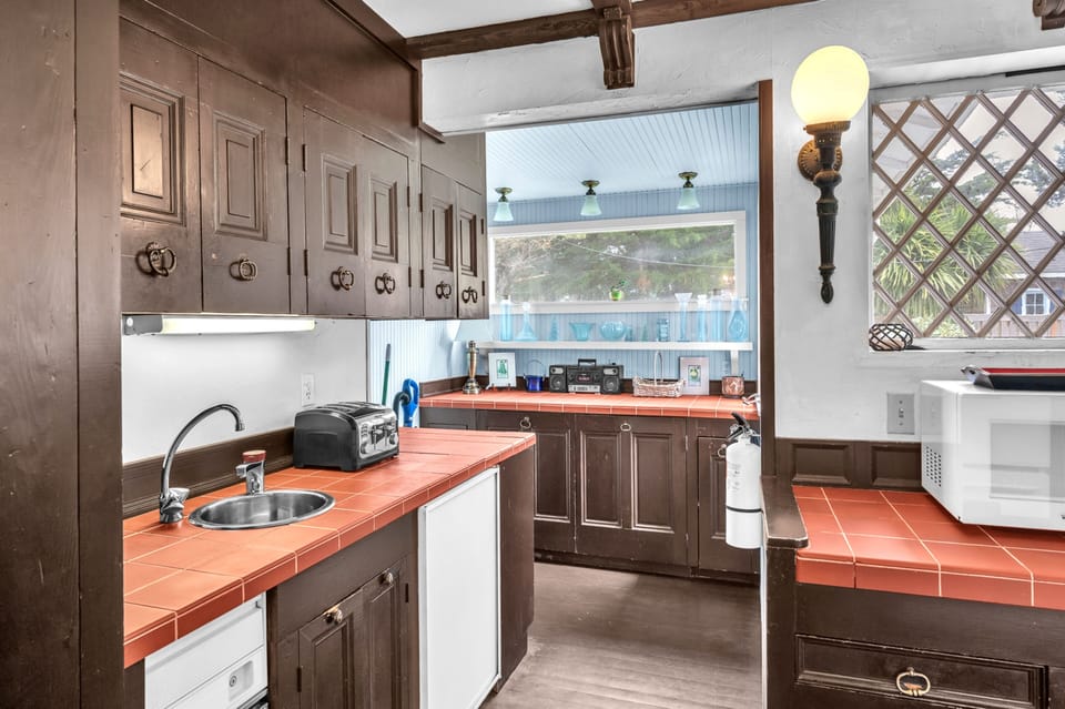 Prepare delicious meals in this spacious kitchen featuring terra-cotta tile countertops, rustic wood cabinets, and charming exposed beams overhead.