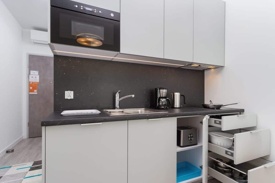  A compact kitchenette featuring a sleek grey countertop, cabinets, and a microwave. The space is well-organized for efficient cooking.