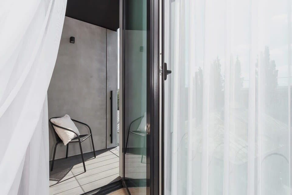 A balcony with a small table and two black chairs, enclosed by a glass railing. The view overlooks the city, offering a peaceful outdoor space.