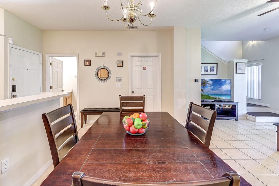 A clear glass bowl filled with apples and oranges sits on the dark wood dining table under a brass chandelier.