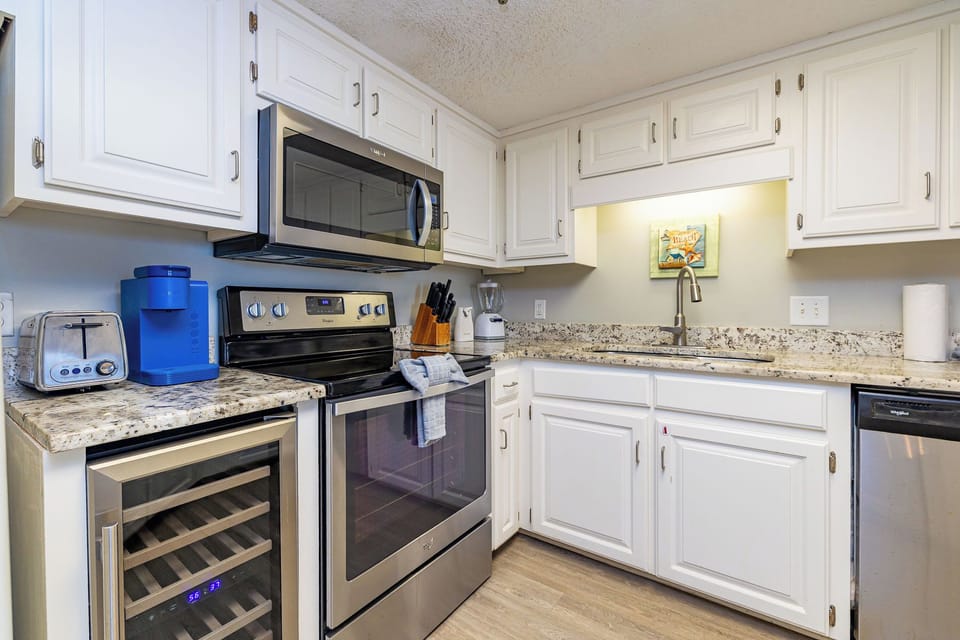 Bright white cabinetry complements the marbled countertops in this kitchen featuring a wine cooler, coffee maker and Keurig