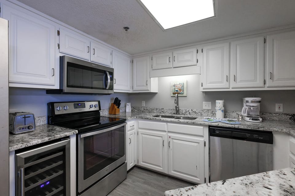Bright white cabinetry complements the marbled countertops in this kitchen featuring a wine cooler, coffee maker and Keurig