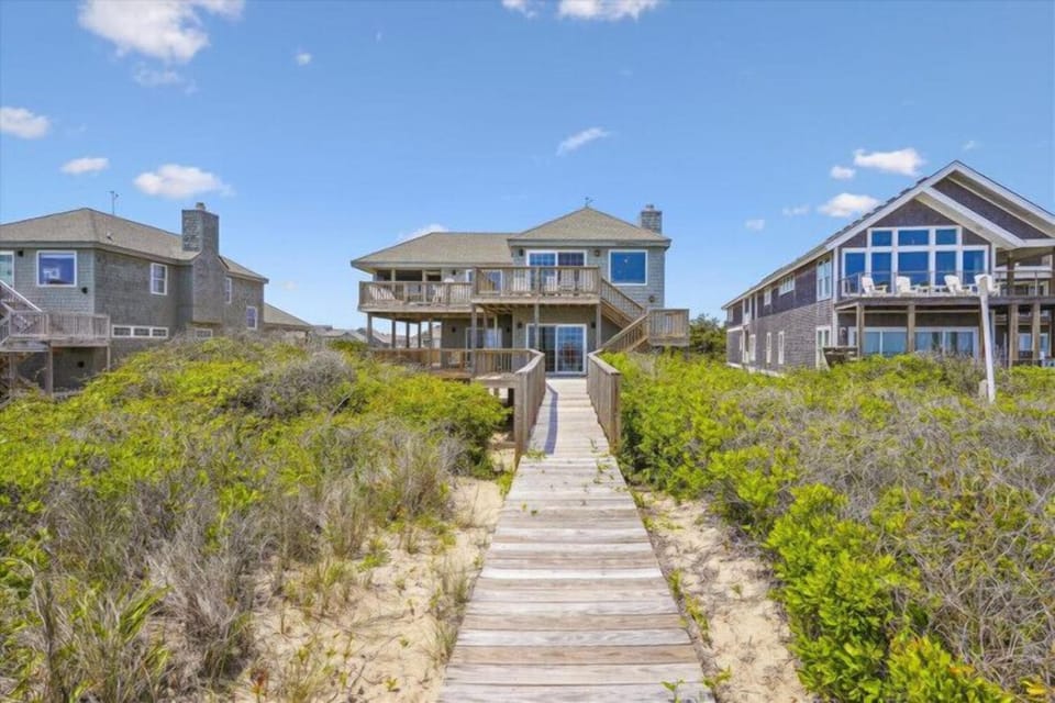 Private boardwalk winds through coastal dunes to oceanfront beach houses with expansive decks and stunning views, perfect for a peaceful seaside retreat.