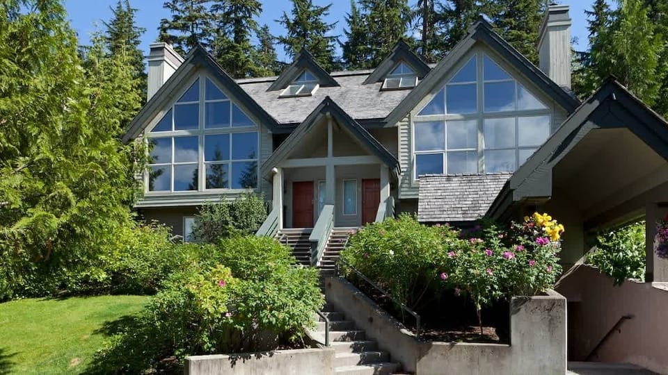 - Elegant mountain home framed by gardens and towering evergreens  
- Expansive windows fill the space with natural light and scenic views  
- Inviting alpine setting blending modern comfort with mountain serenity  