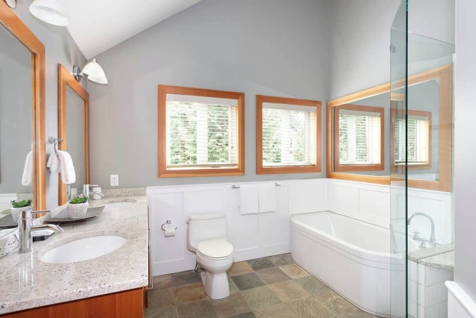 - Bright bathroom with soaking tub, glass shower, and granite vanity  
- Large windows fill the space with natural light and forest scenery  
- Modern fixtures meet cozy mountain style for a spa-like experience  
