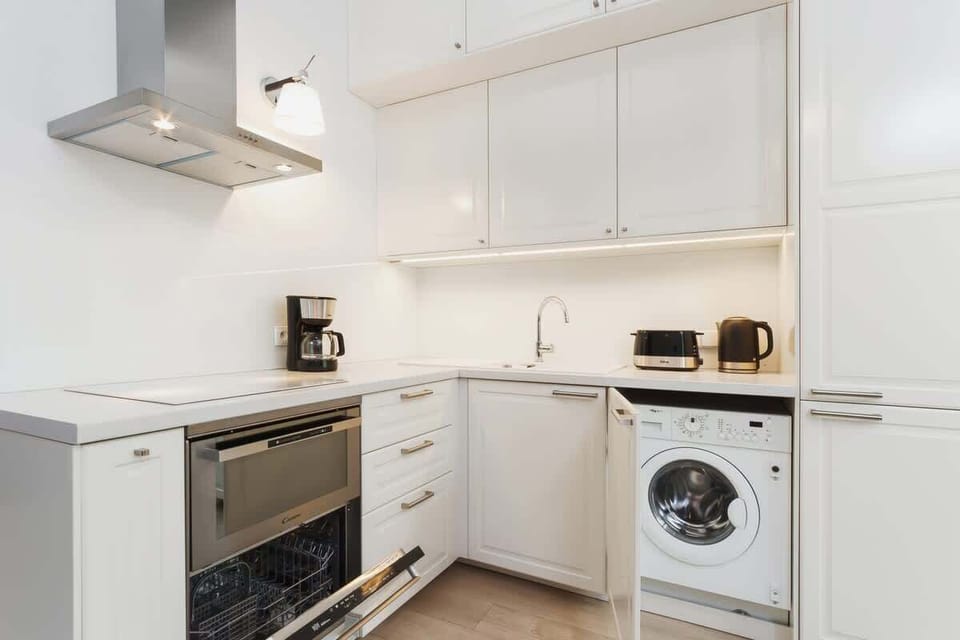 A modern kitchenette with white cabinets, a built-in stove, and a small dining area. The space is well-organized and equipped for basic cooking needs.