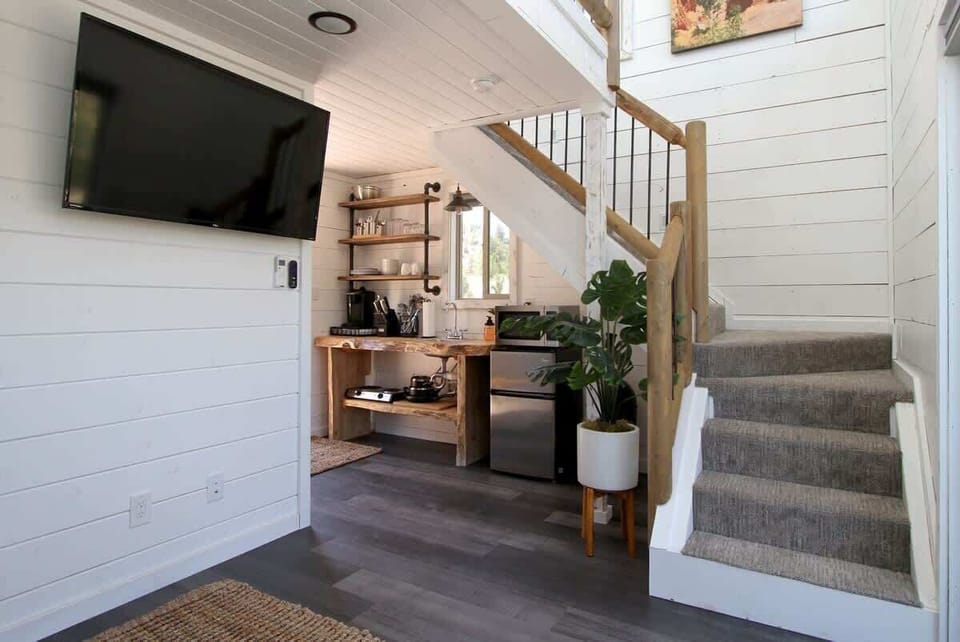 Treetop cabin interior with loft sleeping space, flat-screen TV, private bathroom, kitchenette, and cozy living area.