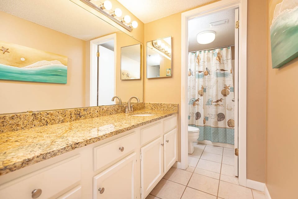 The master bath features a spacious granite countertop, colorful beach-themed decor, and a shower with a charming curtain