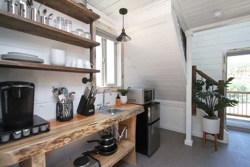Treetop kitchenette with kitchenware, utensils, hot plate, microwave, mini fridge, and coffee essentials for easy meals and snacks during your stay.