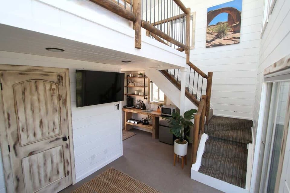 Treetop cabin interior with loft sleeping space, flat-screen TV, private bathroom, kitchenette, and cozy living area.