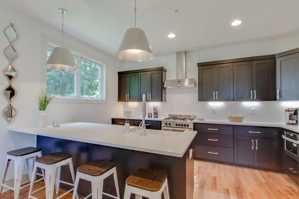 Kitchen with dark wood cabinets, white island with bar stools, pendant lights, and stainless steel range