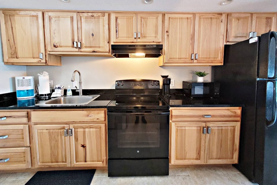 Refrigerator with ice maker, 4 burner stove, oven, microwave, toaster, Keurig coffee maker, cookware, plates, and utensils are provided.
