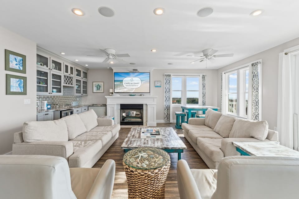 Sink into plush sectional sofas in this bright, airy living space featuring a cozy fireplace and modern entertainment setup.