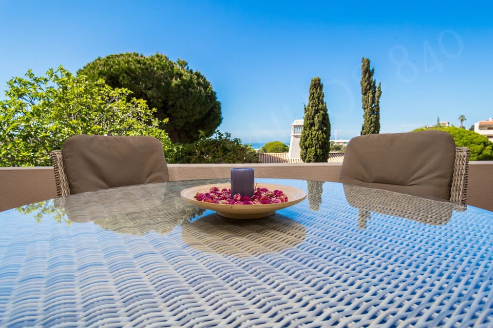 Spacious terrace at Alporchinhos 840 holiday apartment with comfortable outdoor seating, decorative accessories, and views of manicured resort gardens with cypress trees in the Algarve