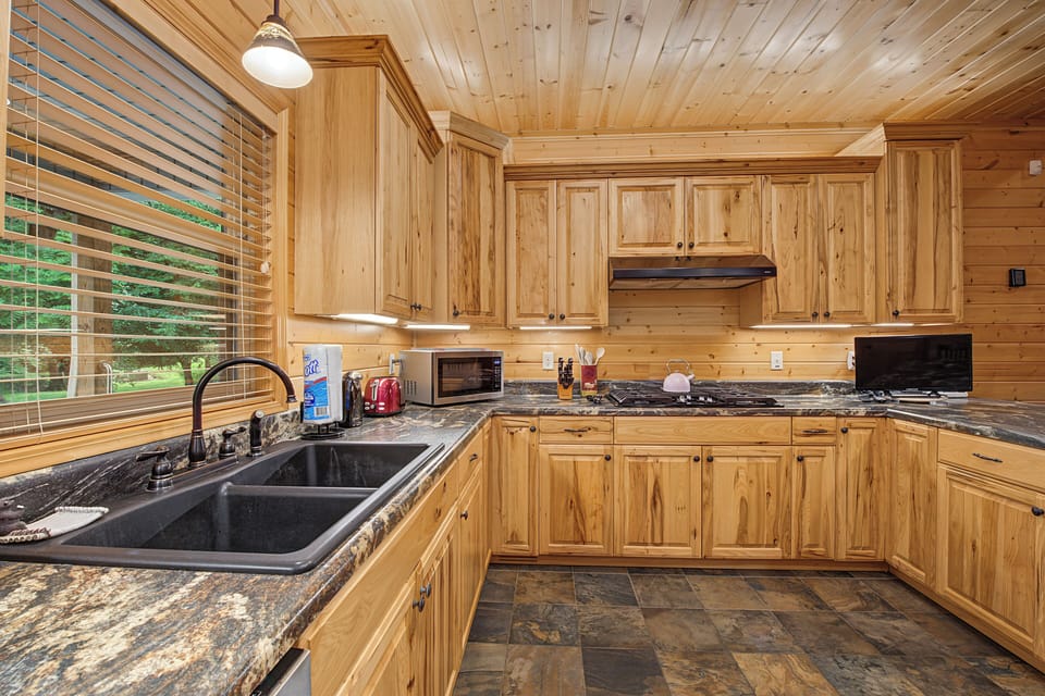 Your fully-equipped kitchen offers warm wood cabinetry, gorgeous granite counters, and modern appliances—perfect for preparing meals while enjoying views of the surrounding greenery through the large window.
