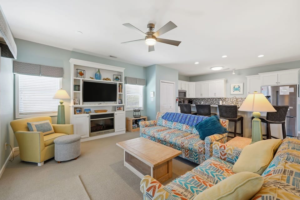 Unwind in your bright, open living space where coastal charm meets comfort. Sink into plush seating, enjoy the built-in fireplace, and savor the airy flow into your fully equipped kitchen.