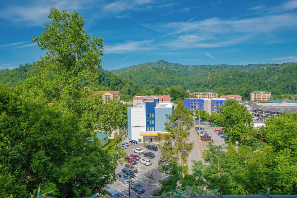 The property sits nestled in a scenic mountain town, with lush green hillsides and neighboring buildings creating a peaceful, vacation-friendly setting.