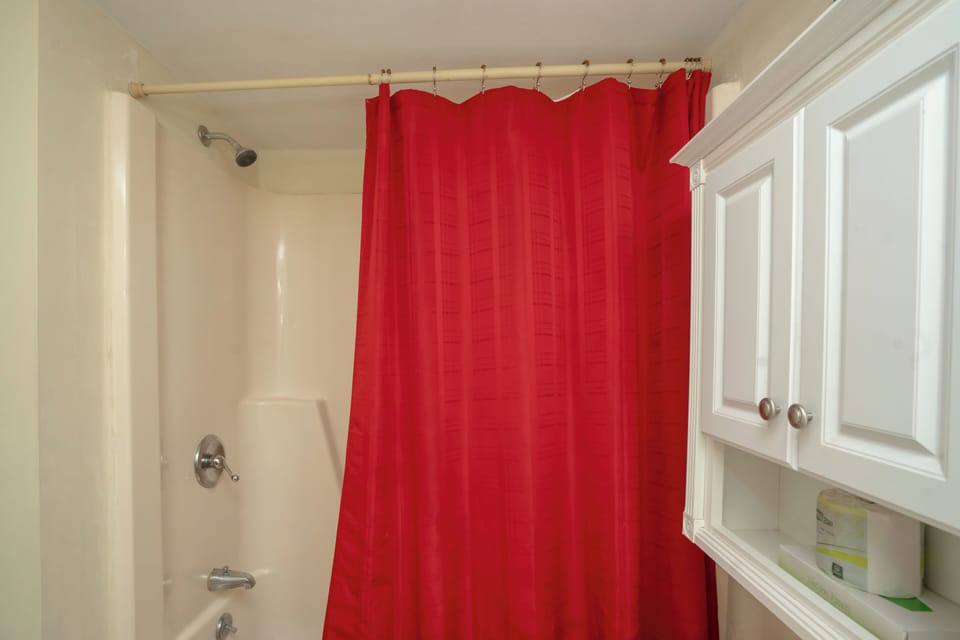 Your private bathroom features a crisp white tub-shower combo with a bold red curtain and thoughtful cabinetry for storing your essentials.