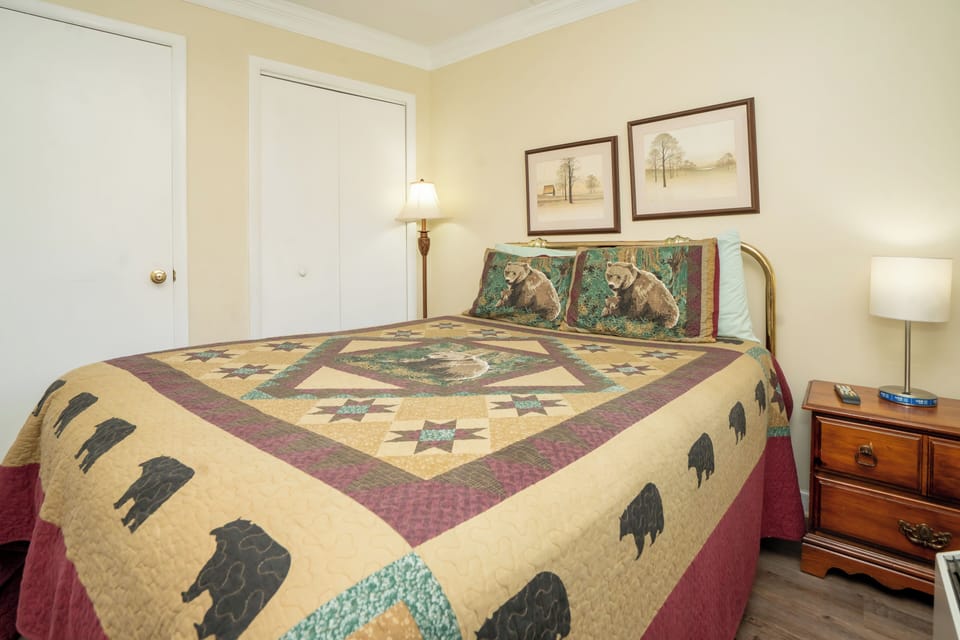 Your cozy retreat with warm tones, a charming quilt showcasing bears, and gentle lighting that creates a restful ambiance—perfect for unwinding after a day of adventure.