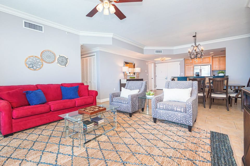 Settle into your inviting living area where a vibrant red sofa and cozy accent chairs await, all flowing seamlessly into your fully equipped kitchen and dining space for effortless beach vacation living.