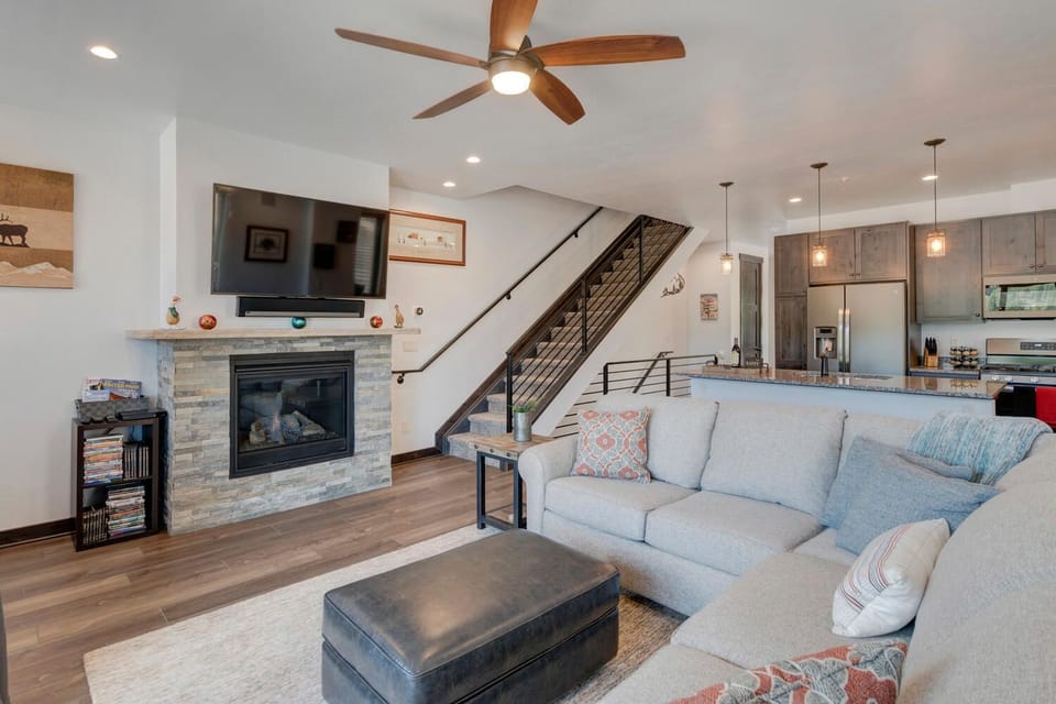 Sectional Sofa, Coffee Table, Ceiling Fan, Fireplace, TV, Staircase, and the Kitchen.