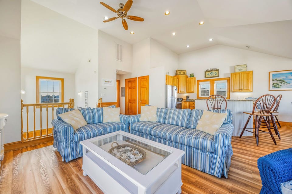 Relax in this bright, open living space where coastal blue-striped sofas invite you to unwind beneath soaring ceilings and warm wood accents.