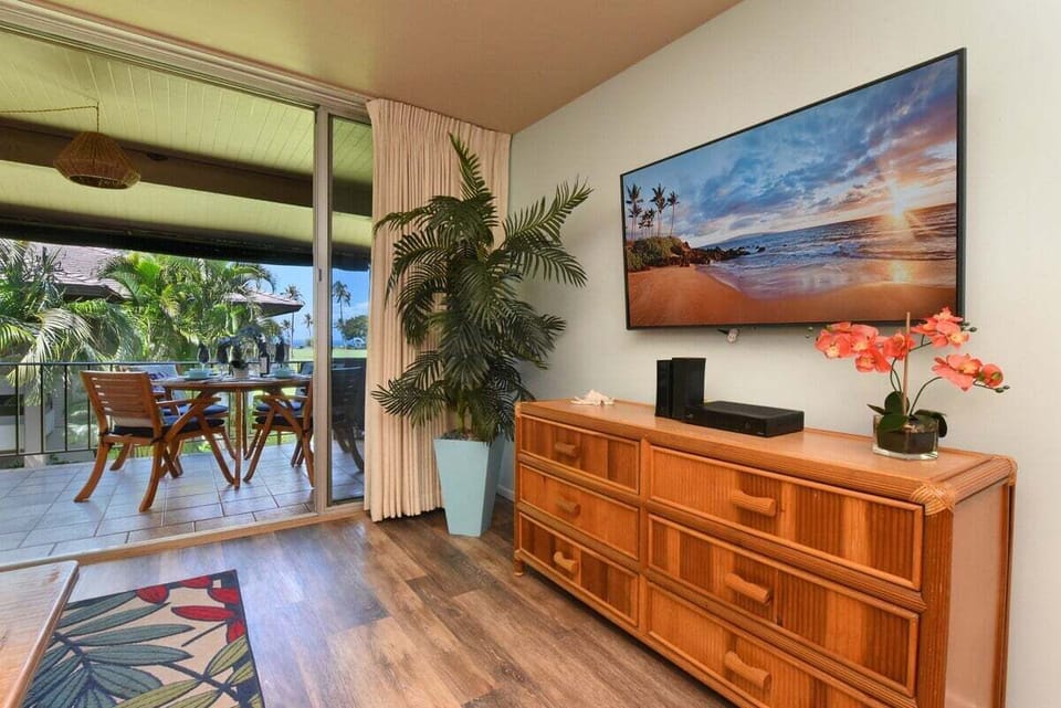 A cozy living space featuring a large TV, stylish dresser, and direct access to a private balcony with tropical views