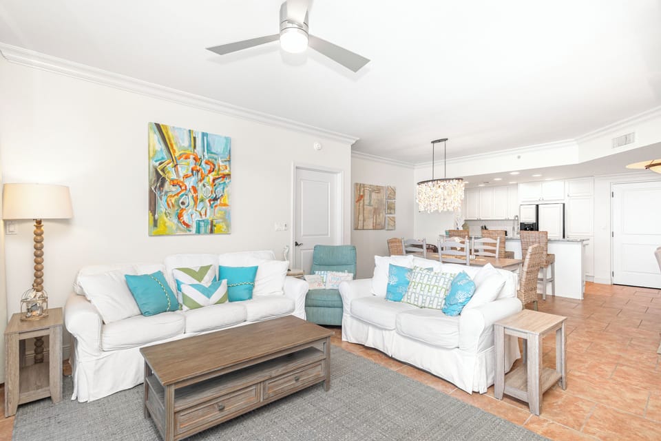 Sink into plush white sofas with colorful accents in your bright, open living space that flows seamlessly into the modern kitchen.