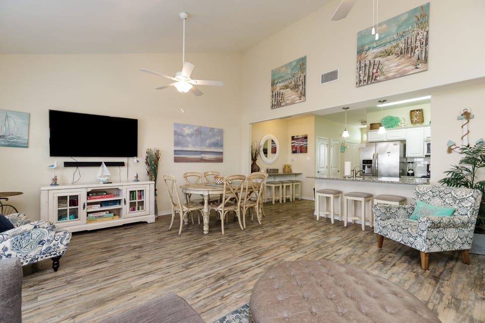 Relax in your spacious open-concept living area featuring coastal decor, modern kitchen, and entertainment center perfect for memorable vacation moments.