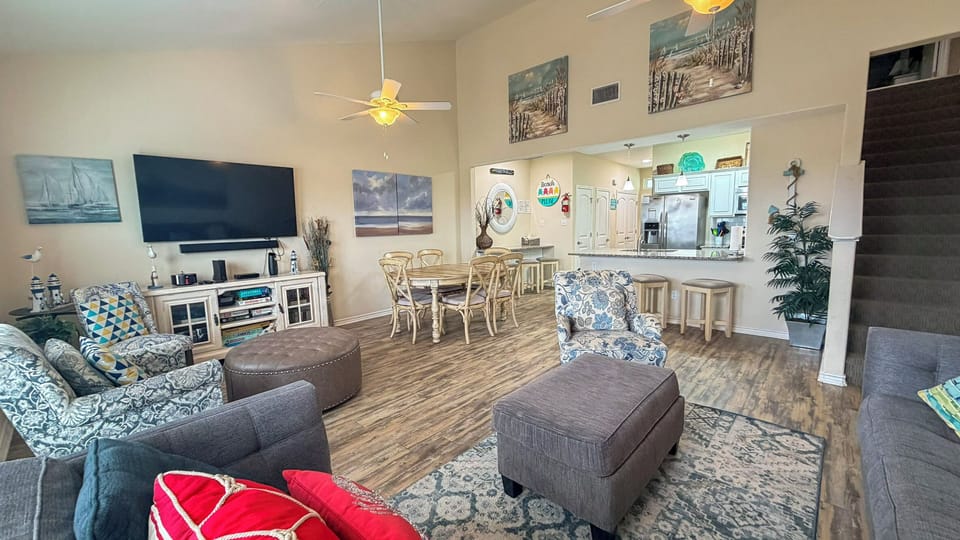 Relax in your spacious open-plan living area with coastal artwork, comfortable seating, and modern kitchen—perfect for unwinding after beach days.