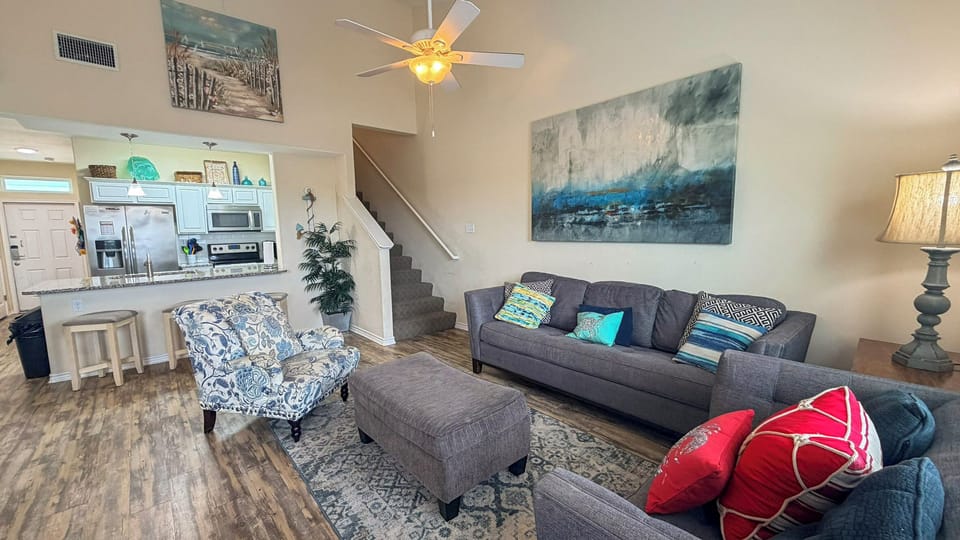 Unwind in your spacious living area with plush seating, coastal artwork, and an open kitchen perfect for vacation gatherings.