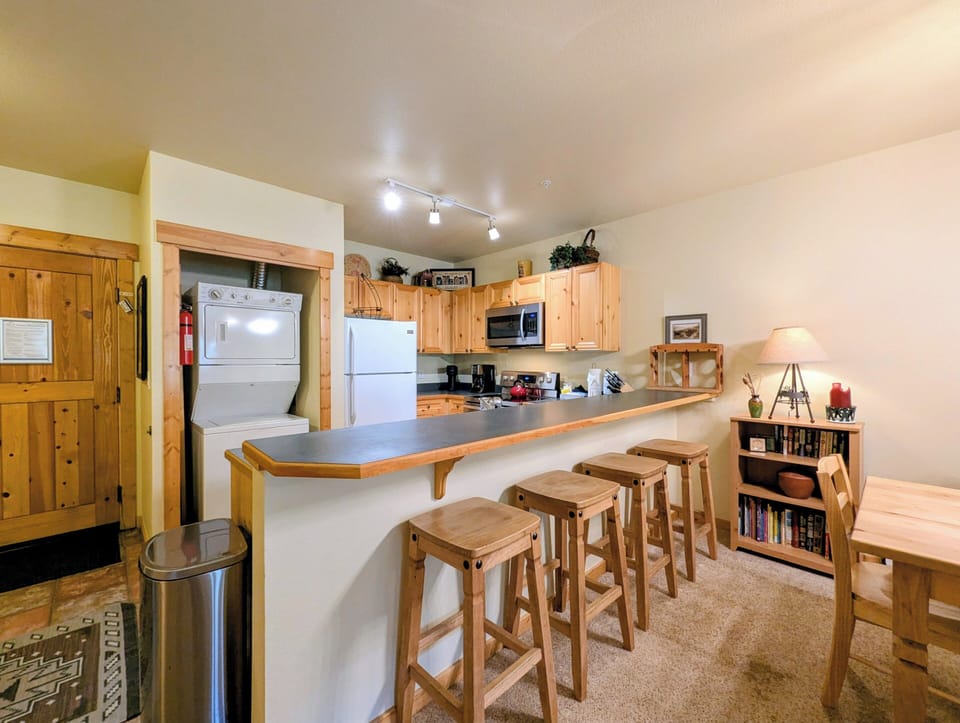 Your cozy kitchen features natural pine cabinetry, full appliances, and a welcoming breakfast bar with rustic wooden stools—perfect for morning coffee or casual meals together.