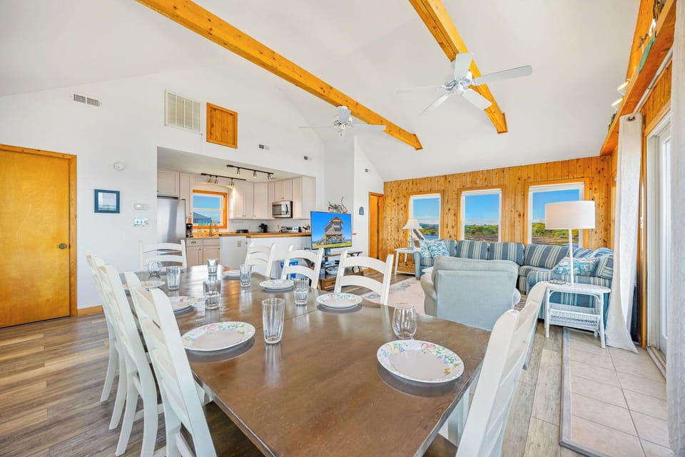 Soaring vaulted ceilings with exposed beams frame your bright open living space, where the dining table invites shared meals and the cozy lounge beckons relaxation with expansive views beyond.