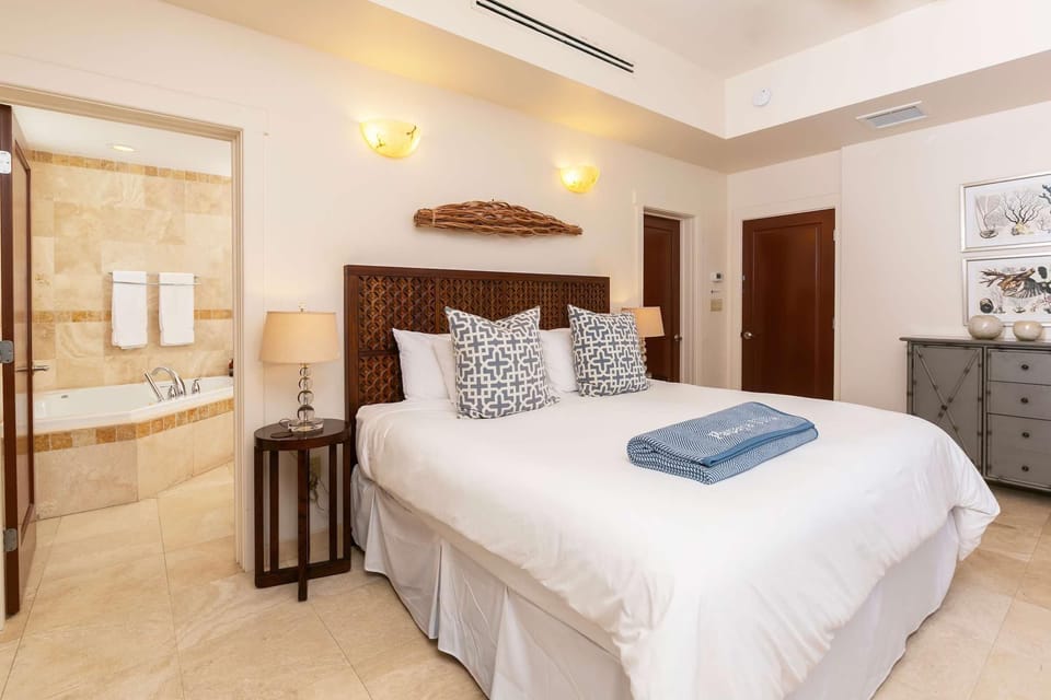 King bedroom features carved wooden headboard, patterned pillows, and adjoining bathroom with tiled soaking tub.