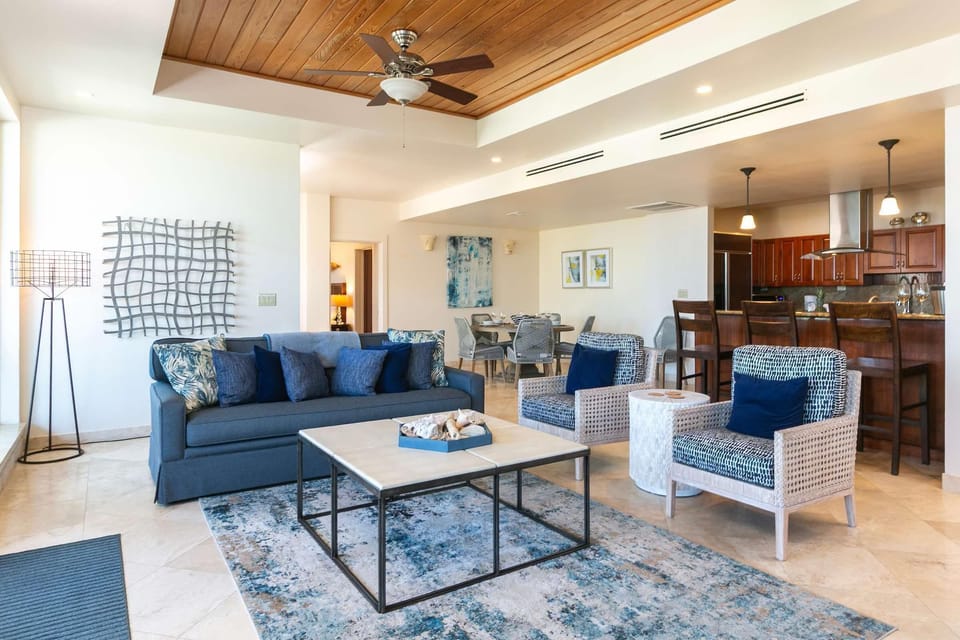 Living area with navy and patterned armchairs, a blue sofa, tiled floors, and a wooden ceiling fan.