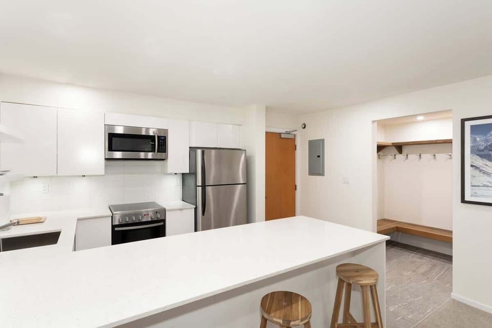 - Modern white kitchen with stainless steel appliances  
- Long breakfast bar with wooden stools for casual dining  
- Fully equipped space for easy home-cooked meals  
