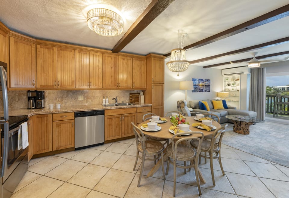 Open-plan kitchen and living area with honey-toned cabinets, tile flooring, and a round wood dining table with seating for six.