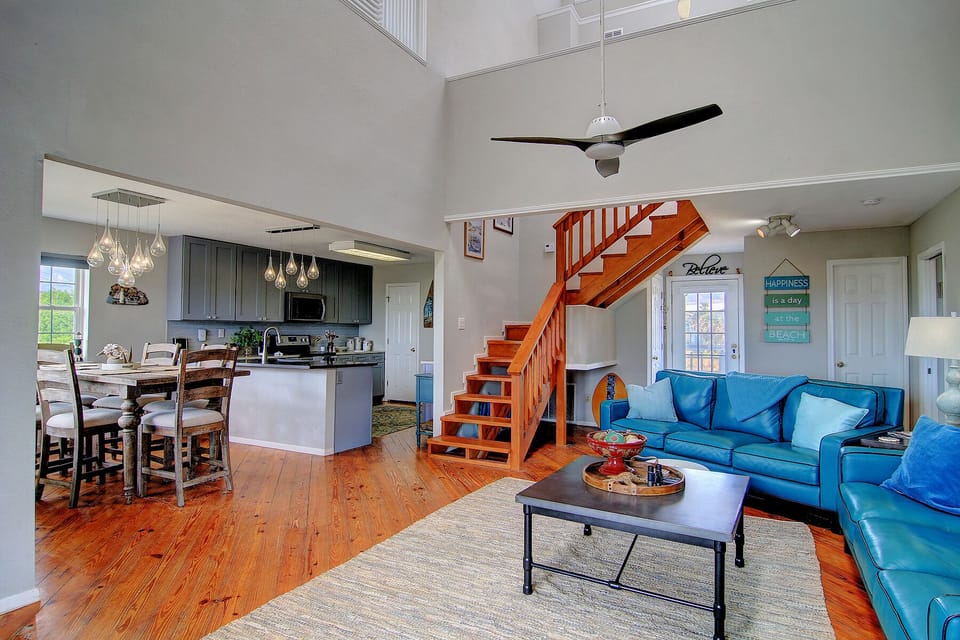 Relax in your spacious open-plan living area with vibrant blue leather seating, modern kitchen, and charming wooden staircase.