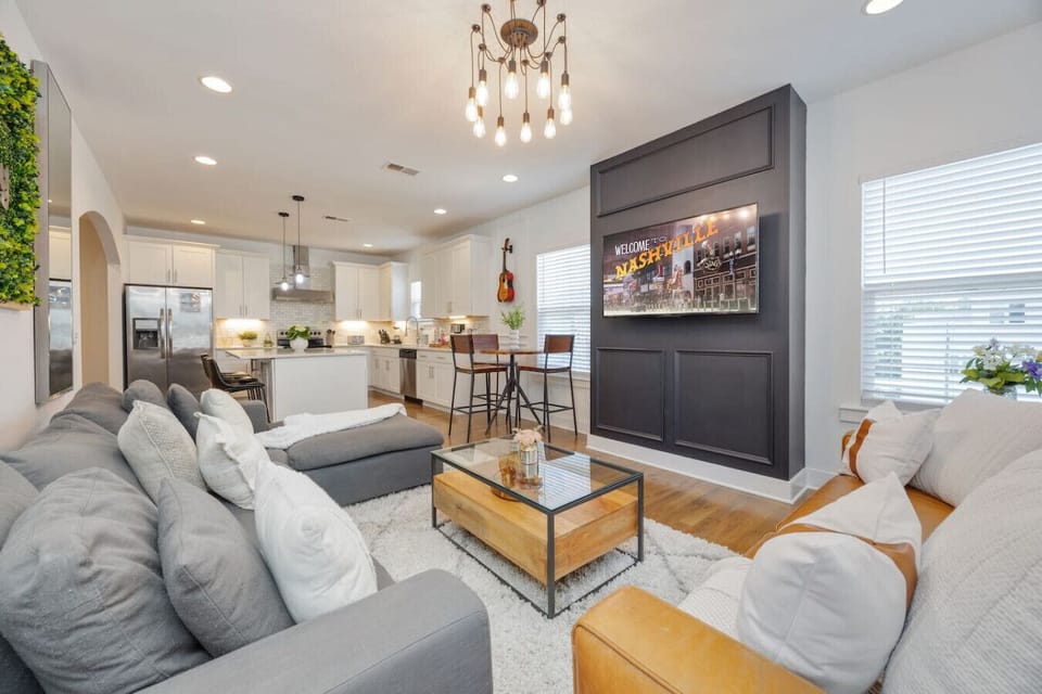 An open living room and kitchen with Nashville print art, a dark accent wall, and modern furnishings.