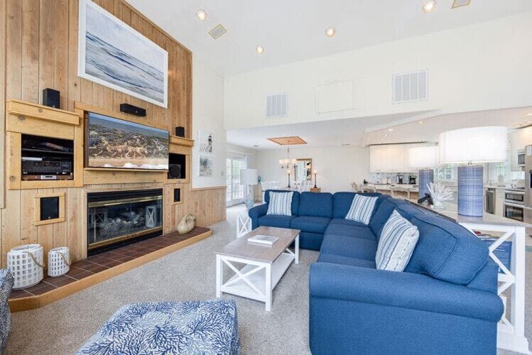 Unwind in your spacious living room with coastal charm, where plush seating and a cozy fireplace invite you to relax after beach adventures, while the open kitchen awaits your culinary creativity.