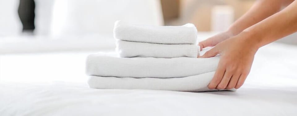 Your fresh towels await on a crisp, made bed—everything ready for your beach escape ahead.