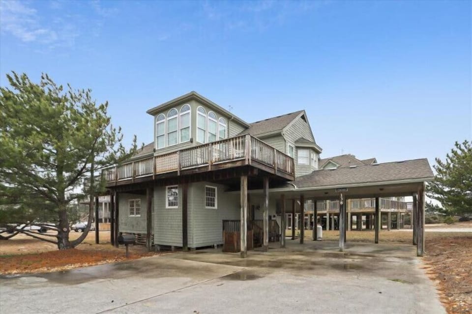 A spacious vacation home featuring elevated decks and covered parking, nestled among coastal pines with clear blue skies overhead.