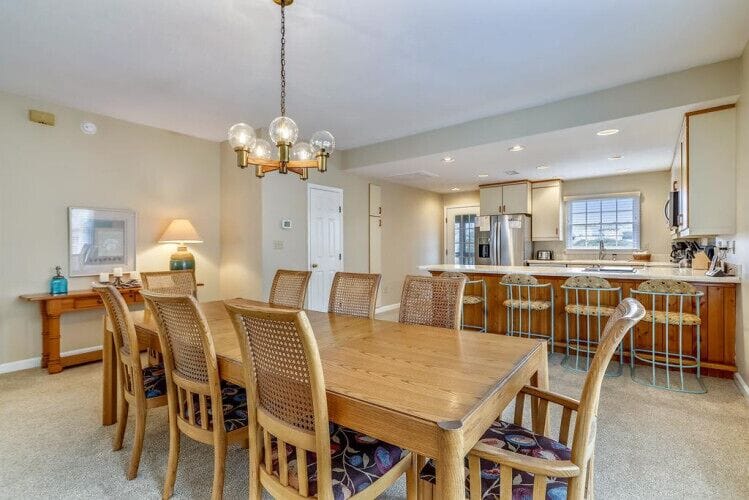 Step into an inviting open-plan space where gathering feels effortless. Your dining table seats everyone comfortably, with warm wood tones and a stylish chandelier overhead, while the modern kitchen awaits your culinary adventures.