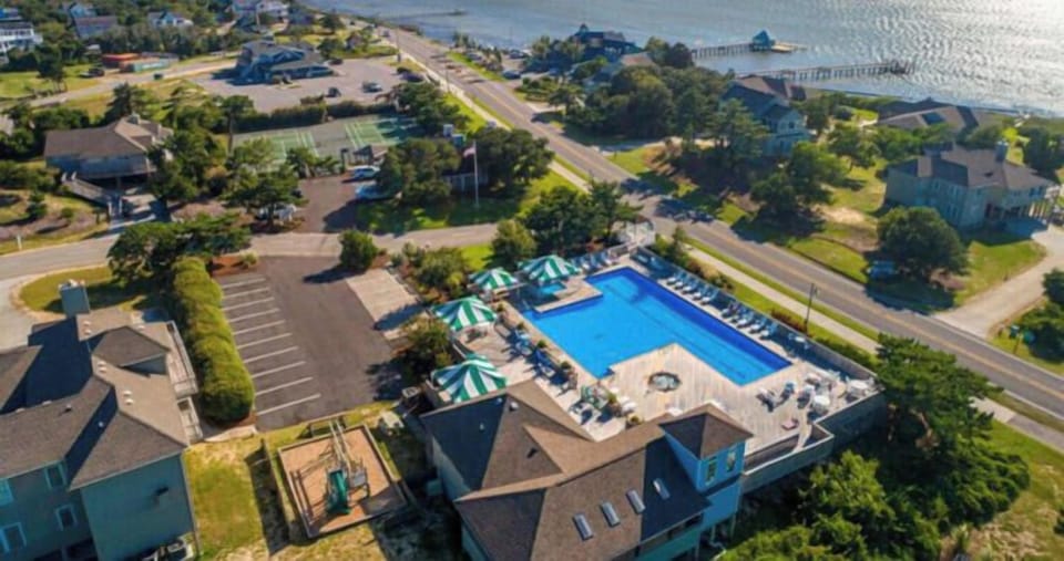 Aerial view showcasing the coastal property, community pool, surrounding neighborhood streets, and nearby waterfront with scenic ocean horizons and residential charm.