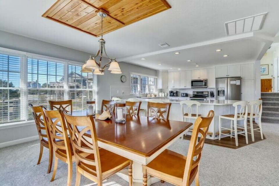 Gather with your loved ones around this stunning dining table that flows seamlessly into a bright, fully-equipped kitchen—perfect for cooking and connecting under the warm glow of wood-paneled ceilings.