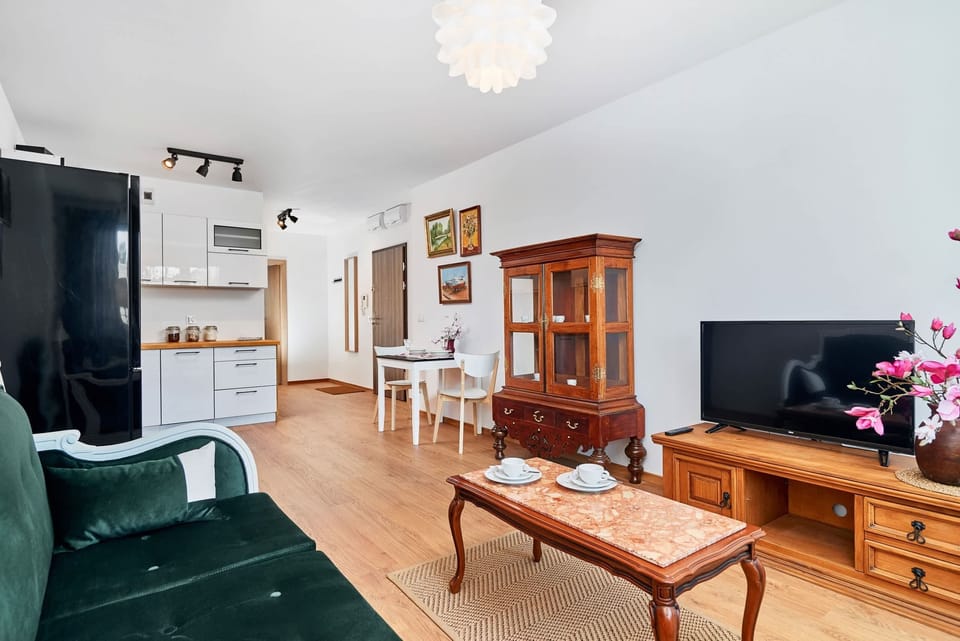 A combined living and dining area featuring a wooden dining table with floral decorations. A large chandelier hangs above, adding elegance to the space.