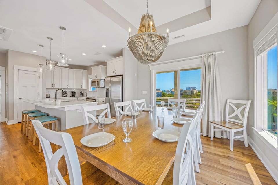 Picture yourself sharing meals at this inviting dining table, with bright natural light and an elegant chandelier overhead. The open-concept space flows seamlessly into a modern kitchen, perfect for gathering with loved ones.
