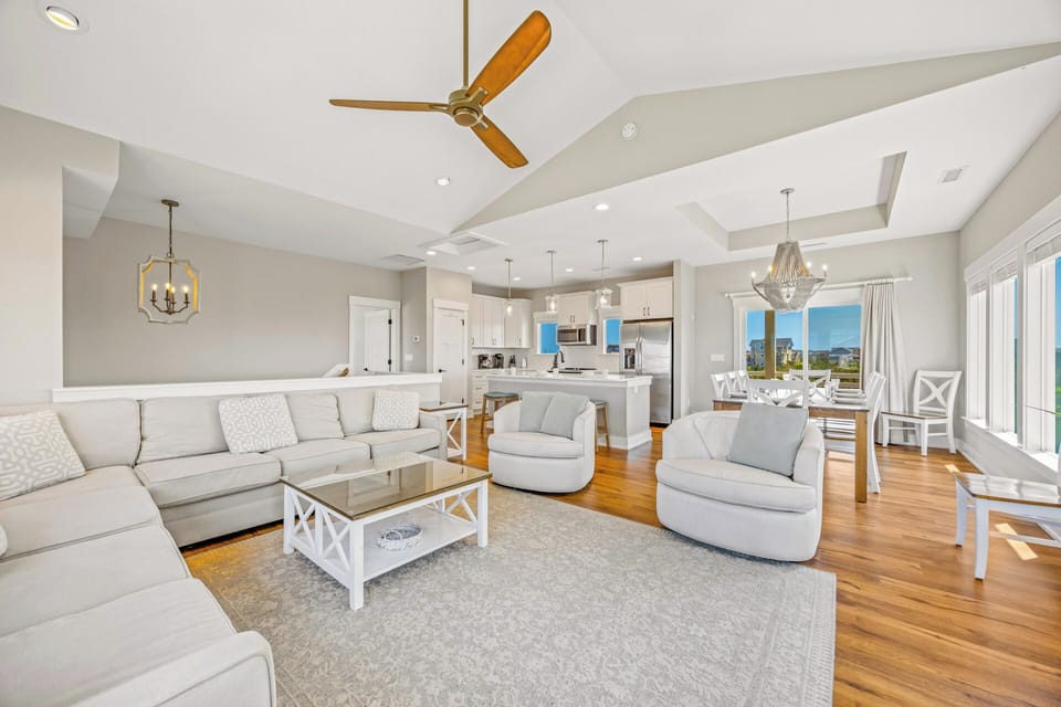 Sink into plush seating in your sun-filled open-concept living space, where vaulted ceilings, warm hardwood floors, and coastal breezes create the perfect retreat after a day at the beach.